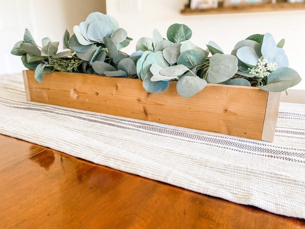 faux eucalyptus inside a wood rectangular centerpiece on a dining table