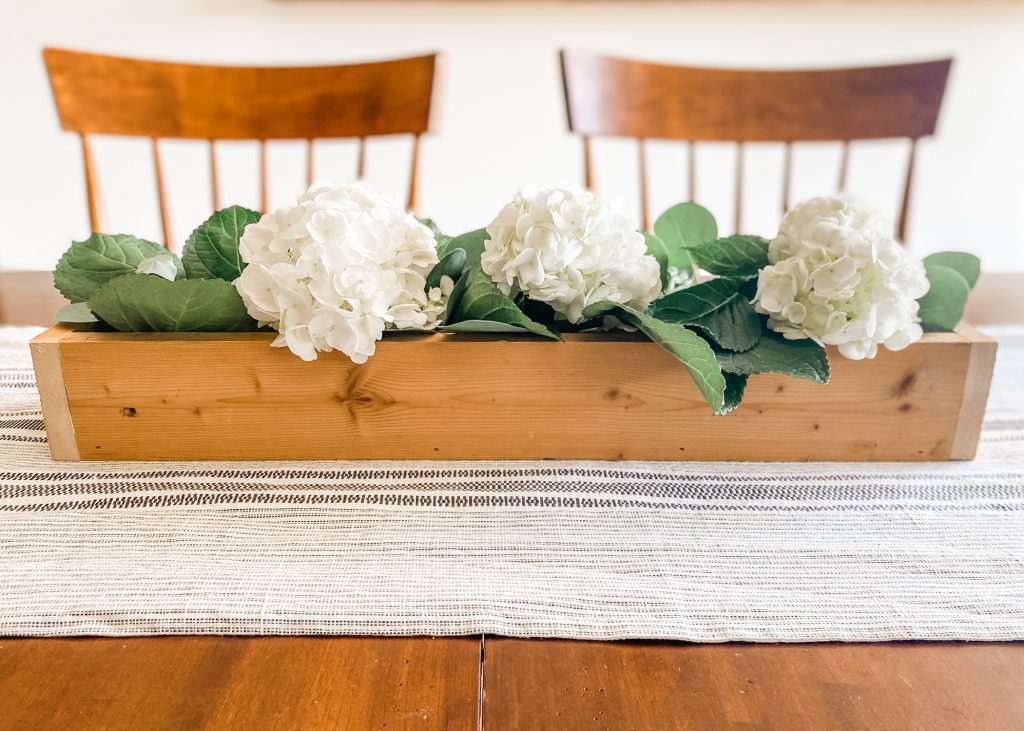 Fresh flowers in wooden box centerpiece on table with runner and two chairs by bloombeautifullyco