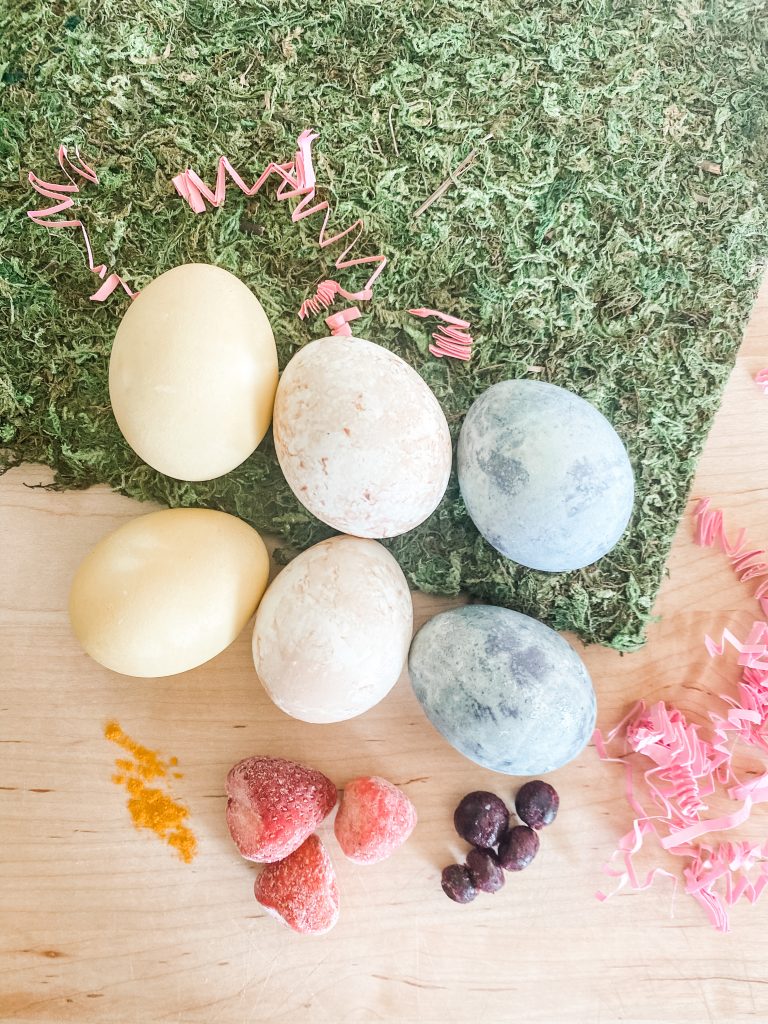 Naturally dyed eggs with turmeric strawberries blueberries on artificial grass and wood board