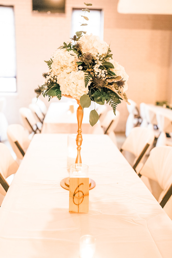 table number 6 stained on piece of wood with candle and tall centerpiece of florals
