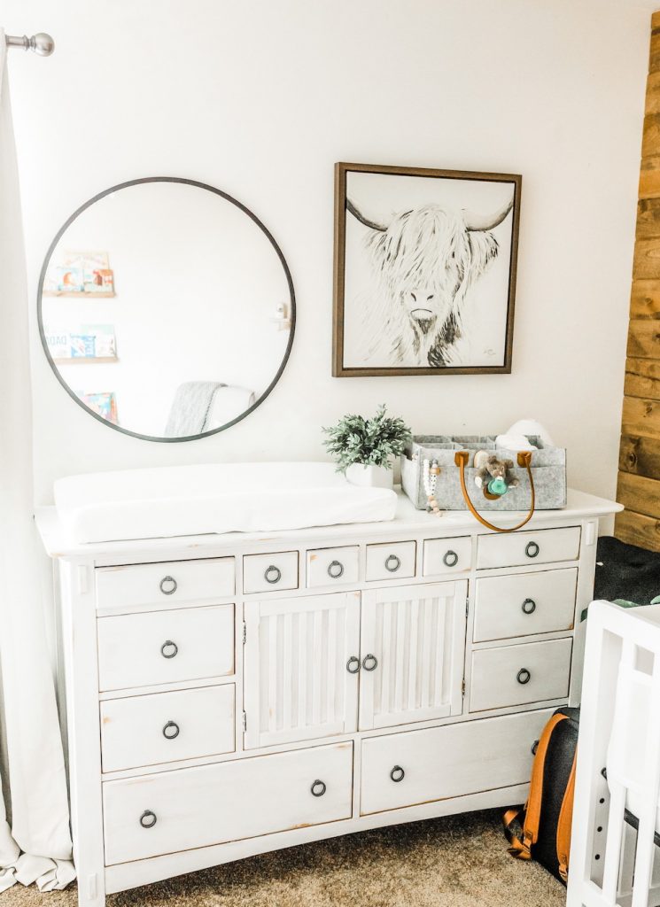white distressed dresser in room with mirror and wall art shown with changing table and tote on top