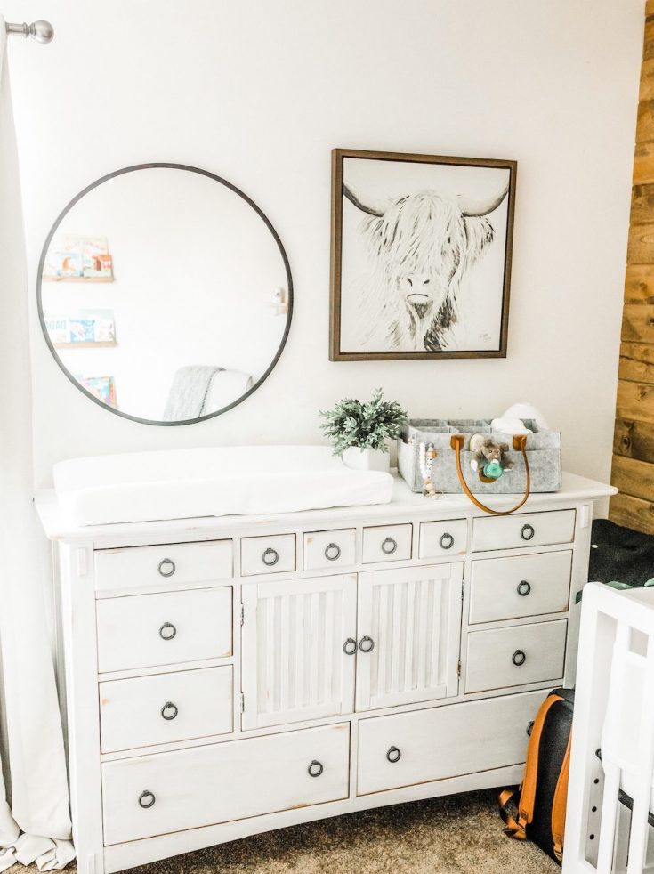 white distressed dresser in room with mirror and wall art shown with changing table and tote on top