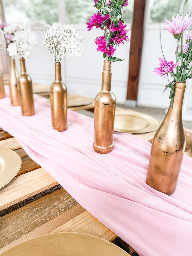 pallet table set with a pink runner and gold wine bottle with pink and white florals