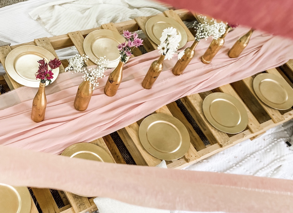 Top view of a pallet table on the floors with chargers, runner, and wine bottles with flowers