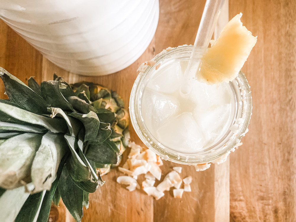 top view of an iced cooler with coconut chips pineapple top and pitcher on cutting board