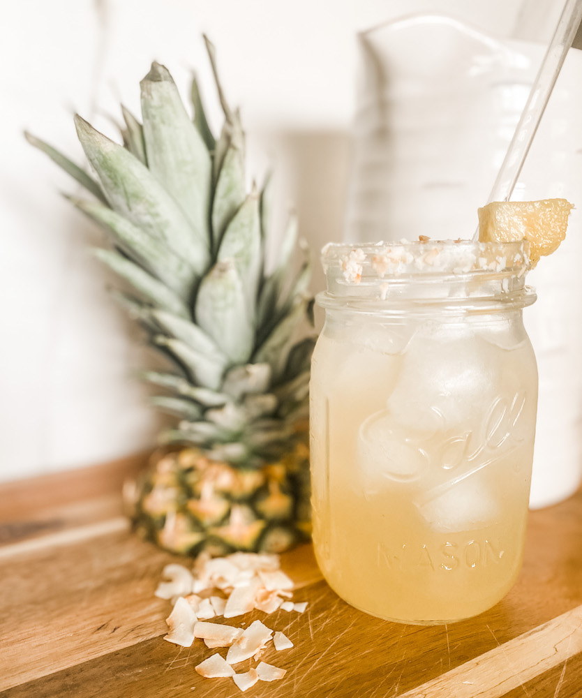 pineapple coconut cooler with coconut crisps pineapple top and pitcher blurred in background