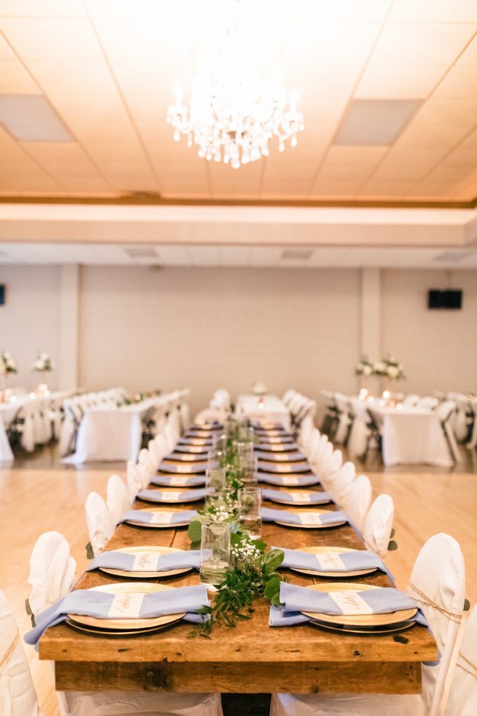 long wood table in middle of room with place settings and chairs with white chair covers