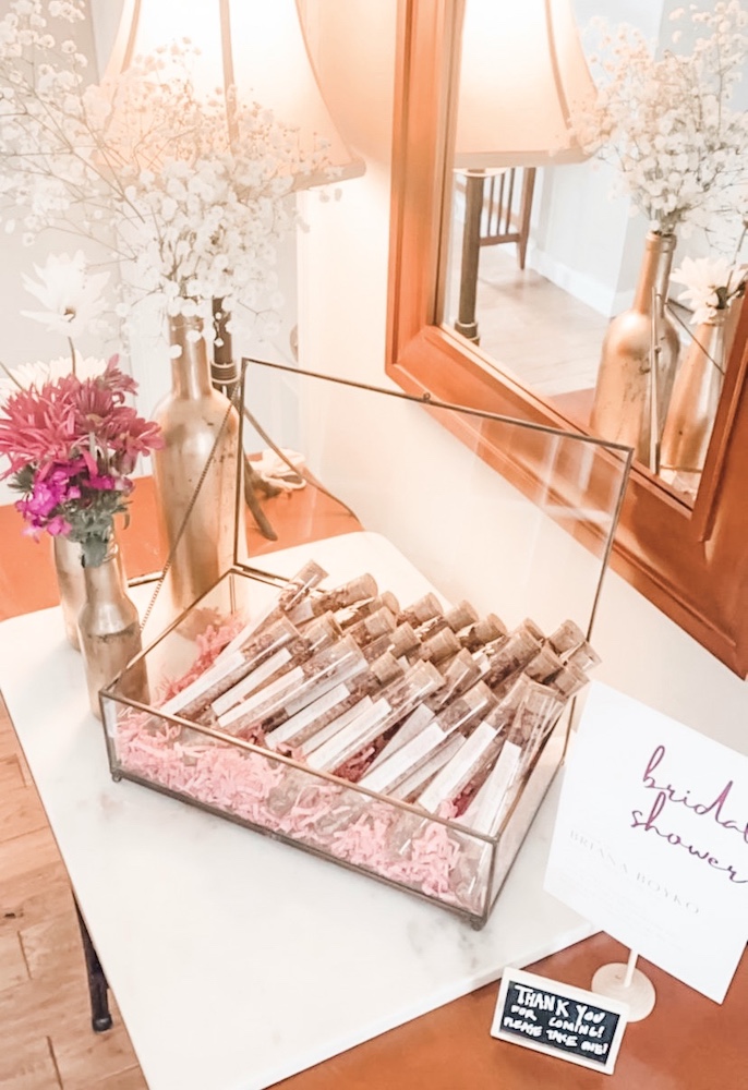 Bath Salt Favors set in a glass case set on a marble surface with bridal shower signs and flowers beside it