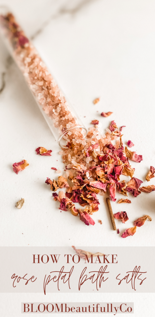 Glass tube with dried roses and pink salt spilled open on a marble surface with Text for how to make rose petal bath salts