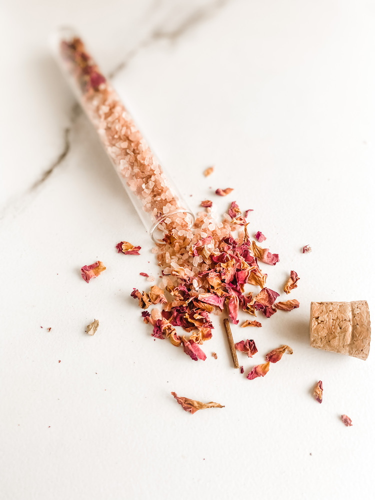 Glass tube with dried roses and pink salt spilled open on a marble surface
