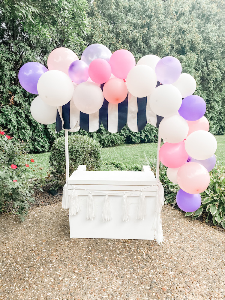 white stand with white and black striped fabric with pink purple and white balloons on top