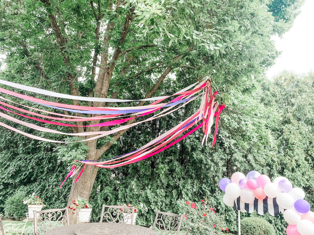 pink and purple streams hung high in trees with a little market stand with balloons in the corner