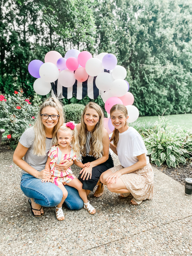 girls smiling in front of a white stand with white and black striped fabric with balloons on top