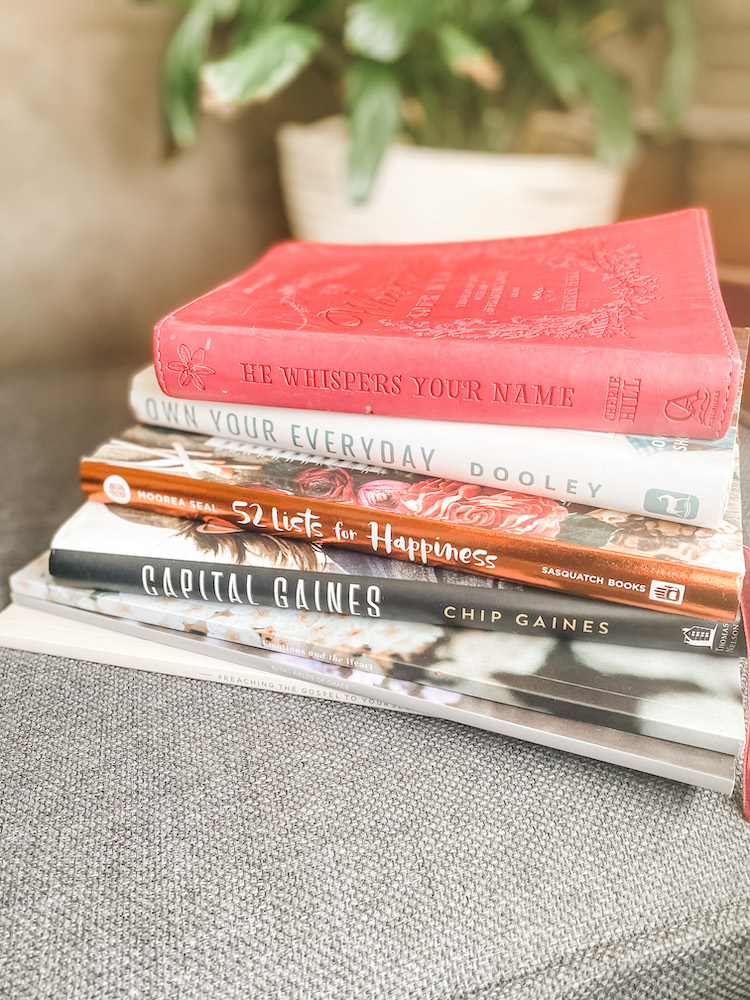 a group of positive books stacked together on a grey stool with a plant in the background