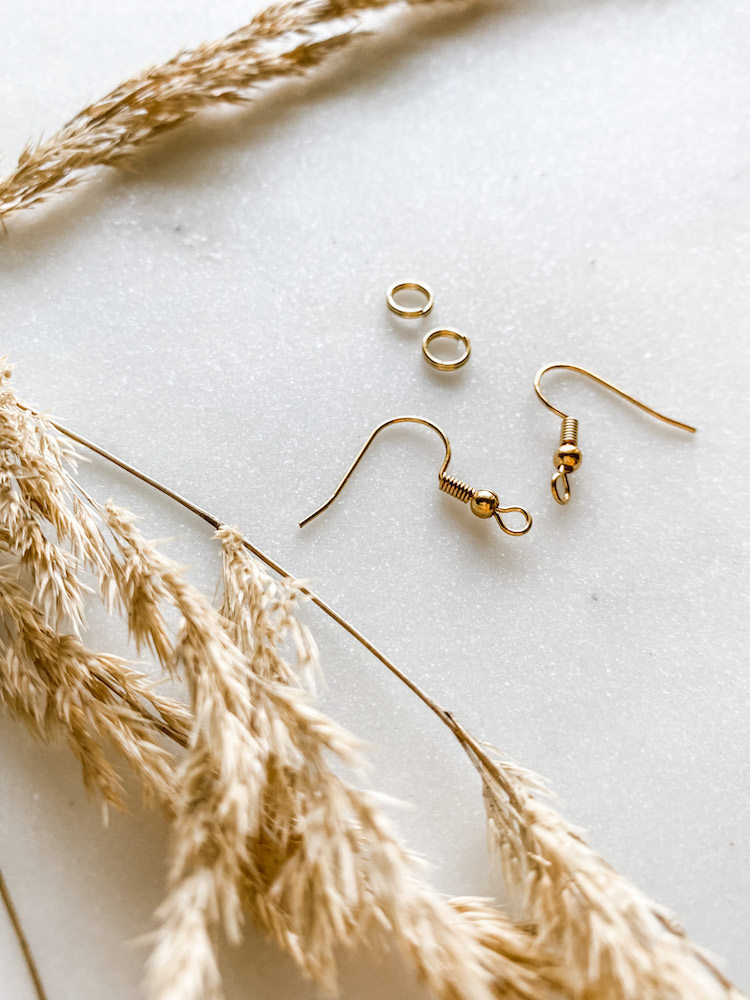 gold earring hooks and earring pieces to make dangle earrings on white surface with dried tan floral