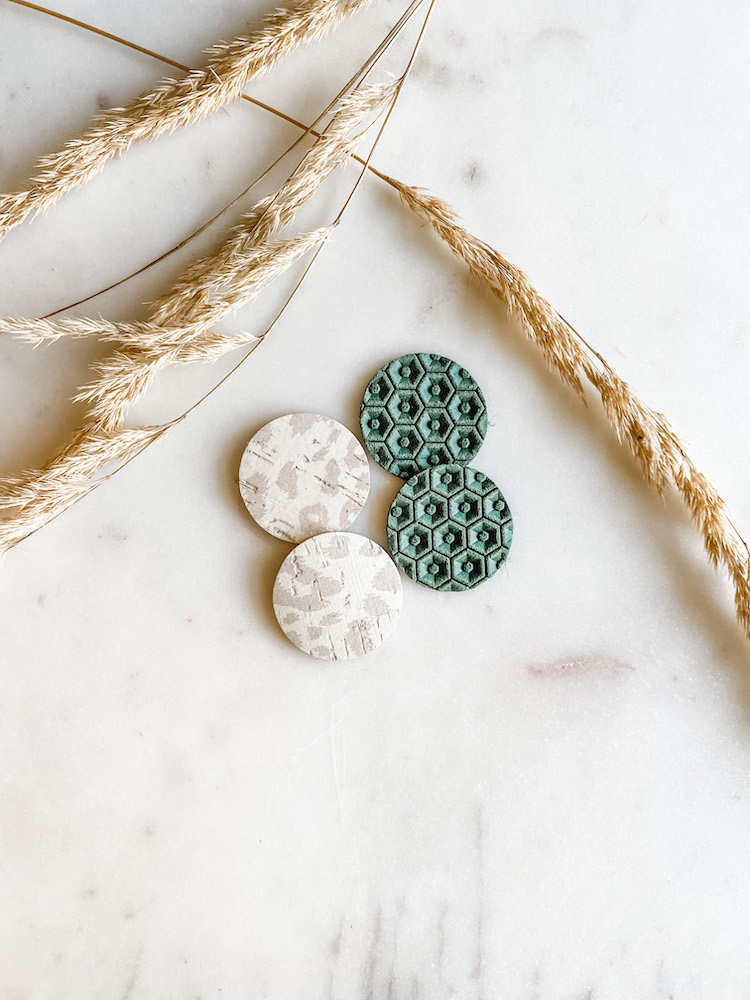 set of light grey and white leopard earrings and a set of dark green circle earring on white surface with brown dried florals