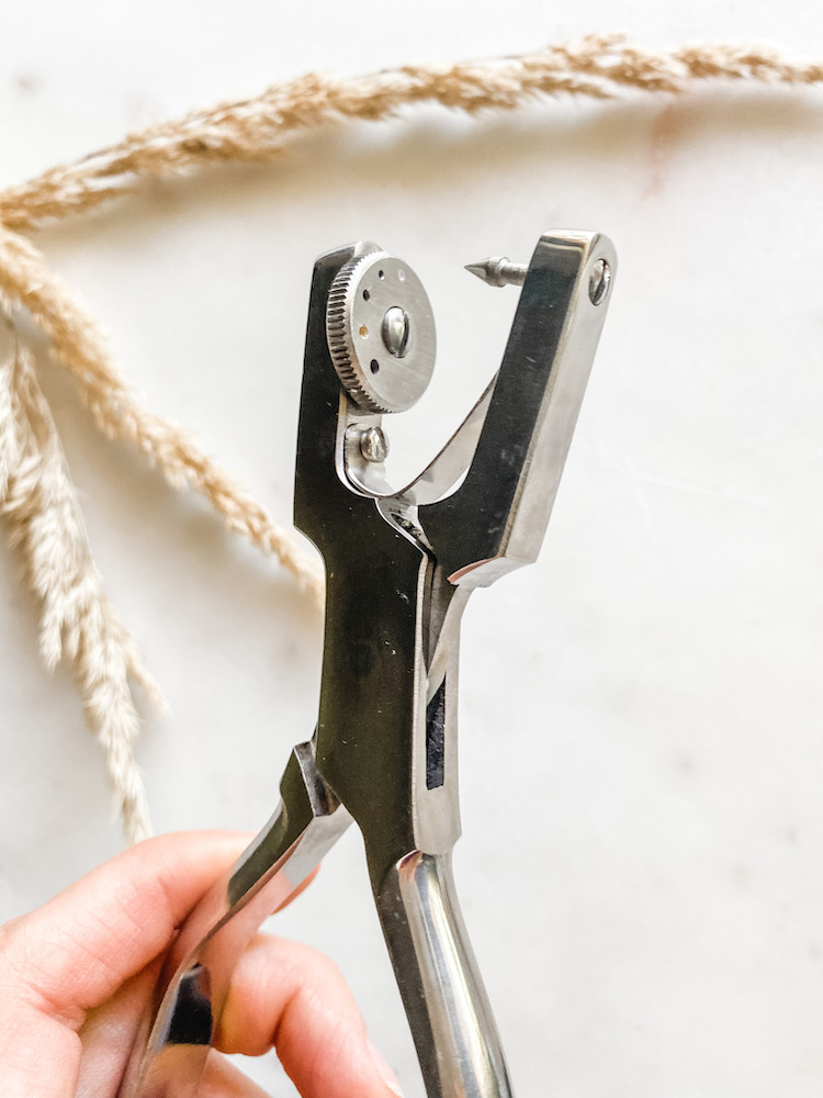 fingers holding a leather punch hole gun with bright background